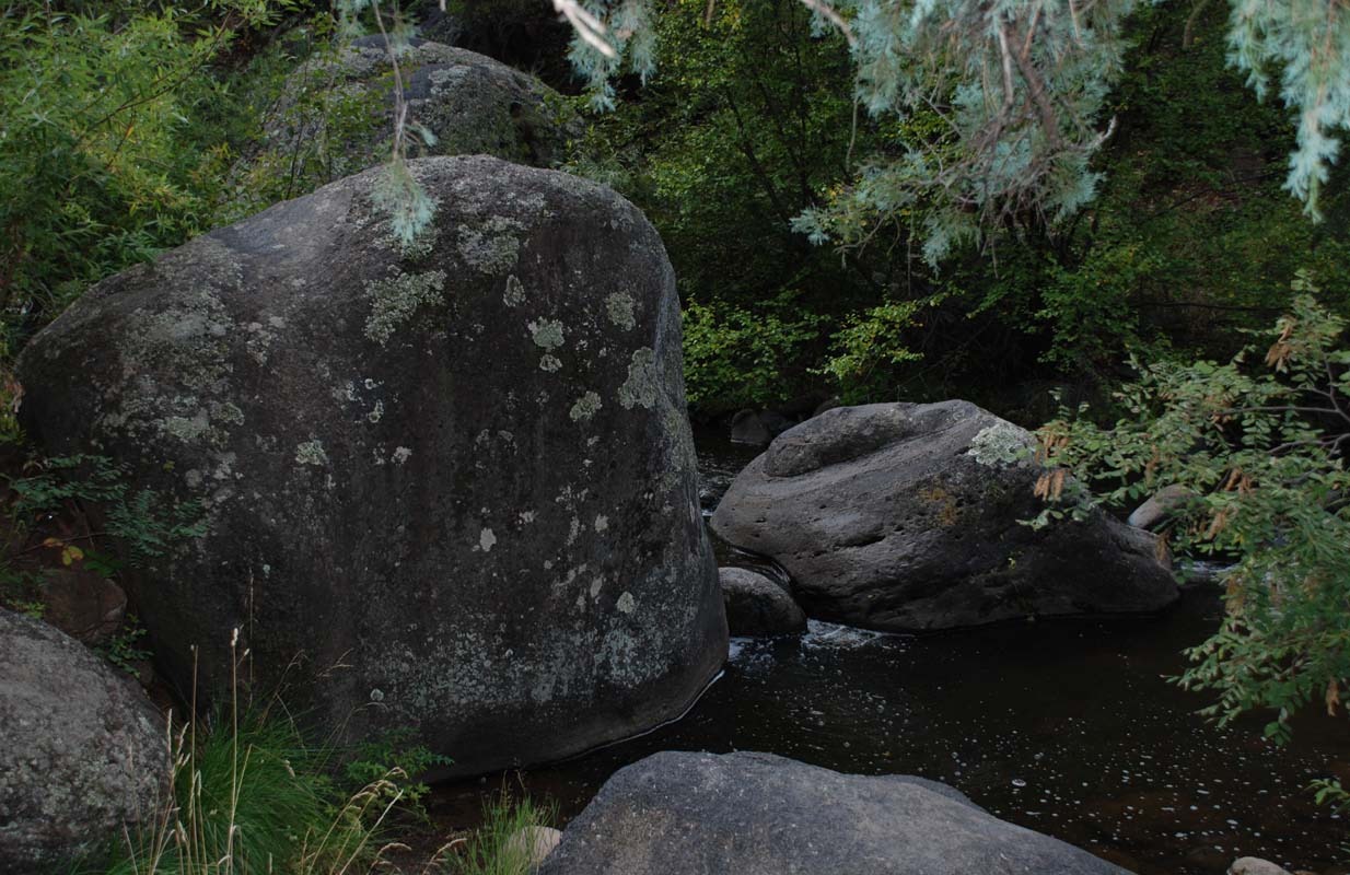 Large, moss-covered boulders frame a tranquil stream, surrounded by lush greenery