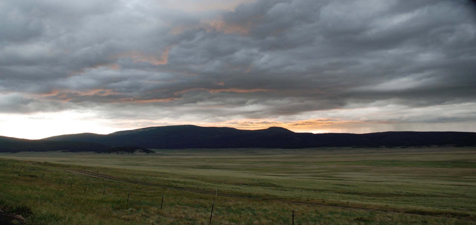 Expansive grassy plains beneath a dramatic sky filled with dark clouds and a hint of sunset,